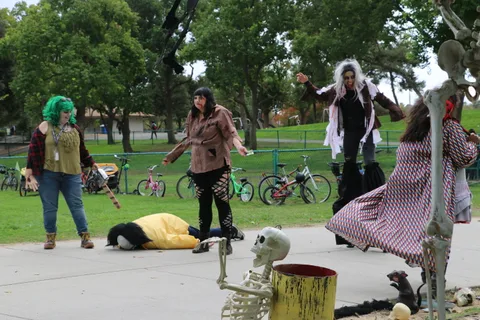 Performers gather near hanging skeleton decorations in the park.