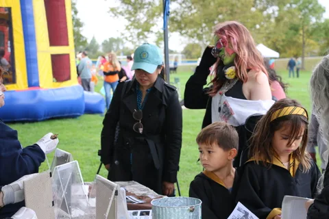 A group including children in black robe costumes stands near a booth.