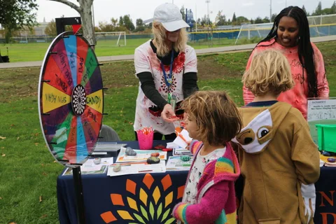 A staff member in face paint hands out prizes to children at a booth.