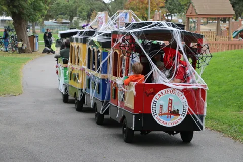 A line of decorated train cars moves down the park path.