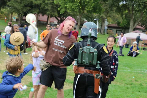 A man in a foundation shirt and another in a full helmet costume pose together with a child nearby.