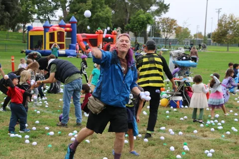 A man throws a ball overhand as a bee-costumed girl watches nearby.