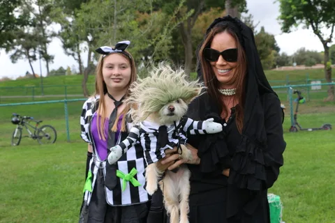 A girl and a woman pose together with a fluffy costumed dog.