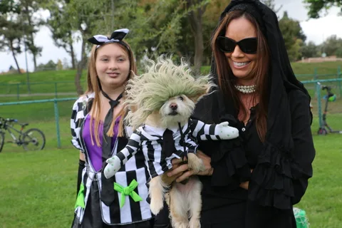A girl holds a costumed dog while posing with a woman in a black lace outfit.