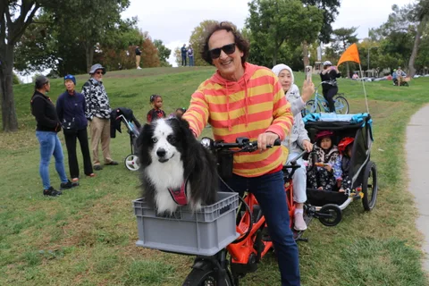A man smiles warmly beside his dog riding in a crate basket on his bike.