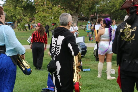 Costumed musicians with trombones stand angled away from the camera.