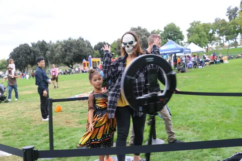 A girl in a butterfly costume and a woman in skeleton makeup stand at an archery range.