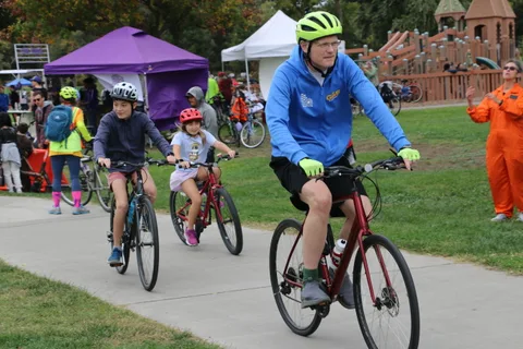 A father and two children in bright helmets ride toward the camera together.