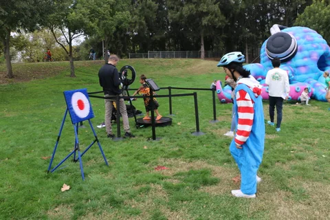 A child in a blue cat costume plays near a giant inflatable creature at an archery range.