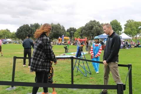 A woman stands at an archery range as a man walks toward the camera.