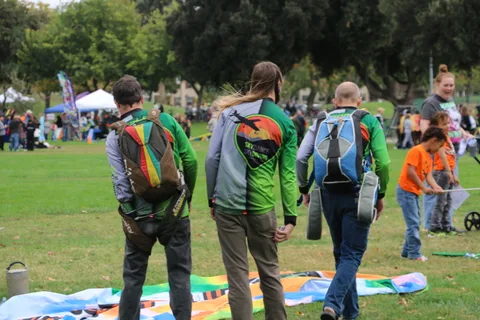 Two men in colorful winged backpack costumes walk while unrolling a large banner.