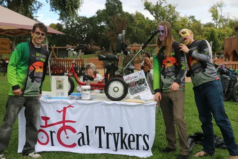 Two people stand by the NorCal Trykers booth with a trike display.