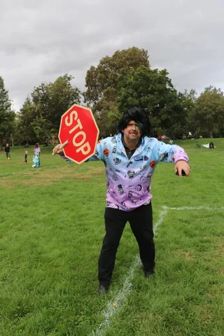 A man in a patterned costume holds up a stop sign while shouting playfully.