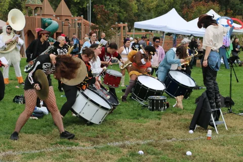 A drummer in skull makeup stands on a stool while the drum line performs beneath tents.