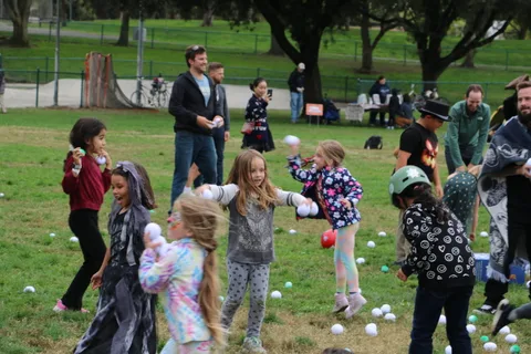 A girl in a tie-dye witch costume reaches for a ball among other kids.