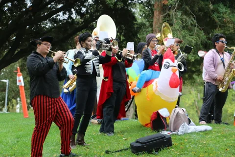 Brass band members play beside a bright inflatable chicken prop.