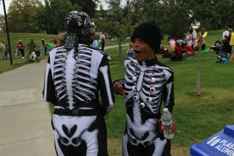 Two people in full skeleton bodysuits walk together, seen from behind.