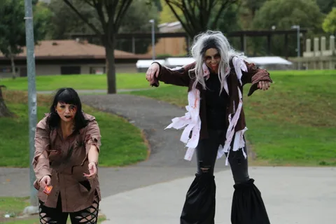 A zombie performer strides forward with arms outstretched on the path.