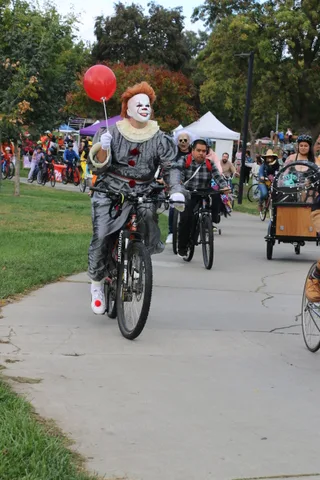 A rider dressed as a menacing clown holds a red balloon while pedaling in the Zombie Bike Parade.