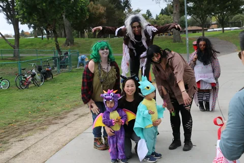 A group photo of costumed performers and two children in dragon and dinosaur costumes.