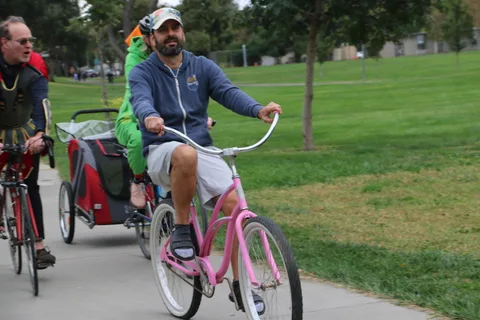A man rides a pink cruiser bike with a cargo trailer past watching kids.