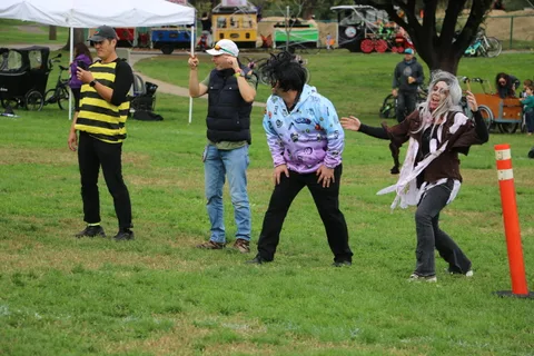 Two costumed figures dance near a tree as onlookers gather at the edge of the frame.