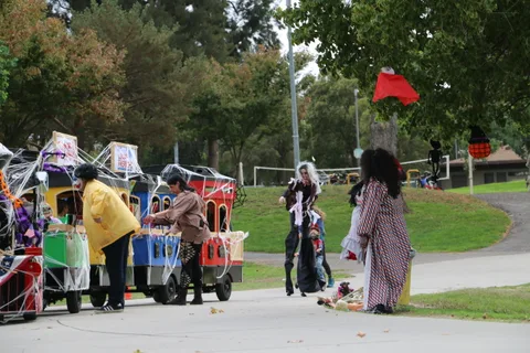 Costumed figures walk near a decorated parade train in the park.