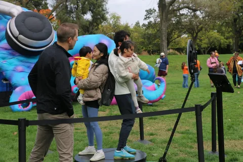 A father carries his daughter in a duck costume as the family walks past a giant inflatable caterpillar.