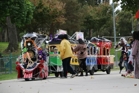 People in yellow jackets stand near a decorated parade train on the path.