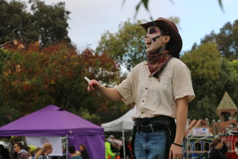 A man in cowboy hat and skeleton face paint grins broadly against a background of trees.