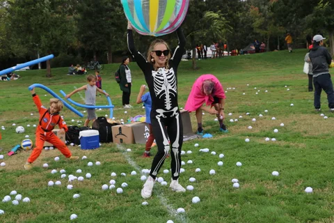 A girl in a skeleton costume leaps into the air during a festival game.