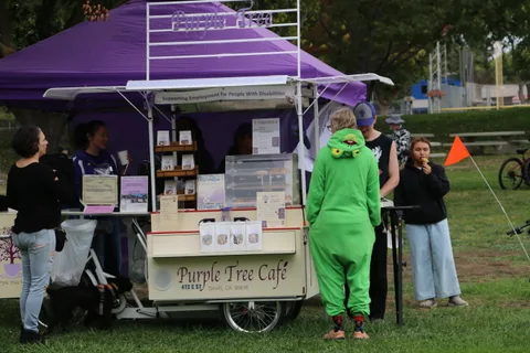 Festival-goers gather near the Purple Tree Cafe booth under a purple tent.