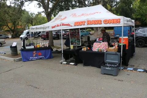 People order at a hot dog vendor tent with a large promotional banner.