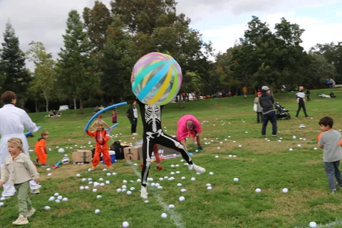 A girl in a skeleton costume jumps as a striped ball soars above the festival field.