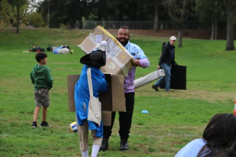 A person in a whimsical oversized cardboard box costume stands among the crowd.