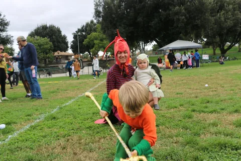 A father in a lobster costume helps his toddler stand among festival-goers.
