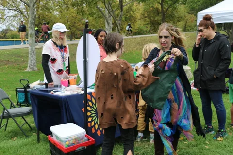 Costumed children gather at a library booth with a blue tablecloth.