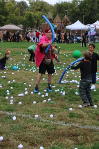 A caped figure swings a foam noodle at kids among scattered play eggs.