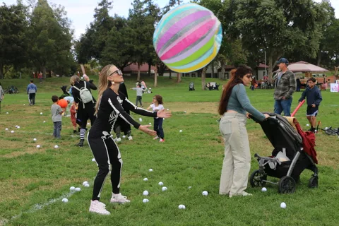 A woman in a skeleton costume throws a colorful beach ball into the air.