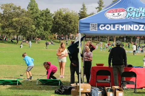 A group gathers at a GolfMindz tent booth in the park.