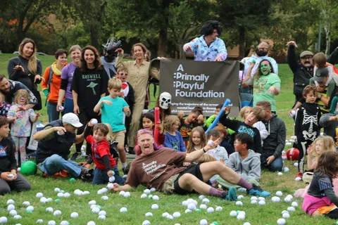 A costumed group poses together in the park with one person stretched out on the grass.