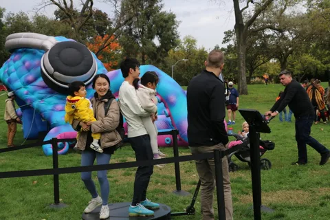 A family walks past a large blue and purple inflatable caterpillar sculpture.