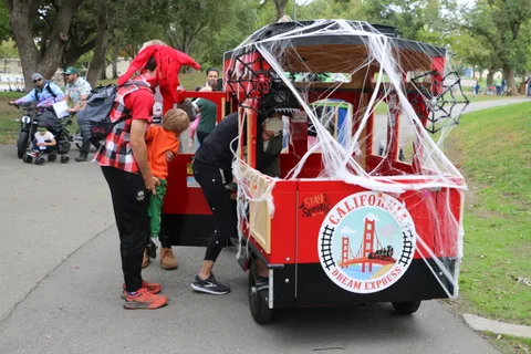 A jester-costumed performer interacts with children near a decorated train car.