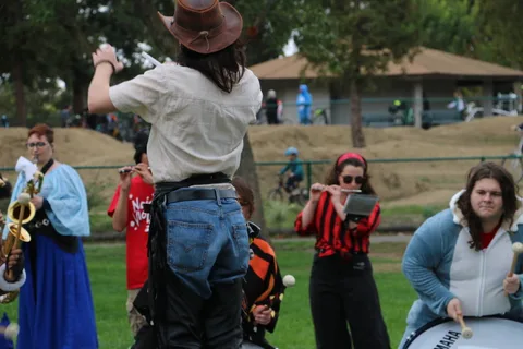 A performer in a cowboy hat raises a drumstick, seen from behind.