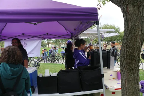 Two staff stand at a purple-canopy booth with equipment cases.