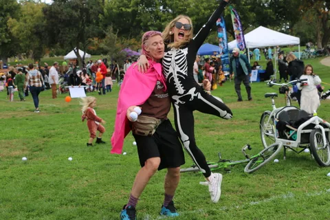 A man in a pink cape poses playfully with a woman in a full skeleton costume.