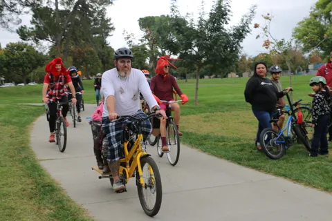 A colorful group of riders, including a child, pedals down the sunny path.