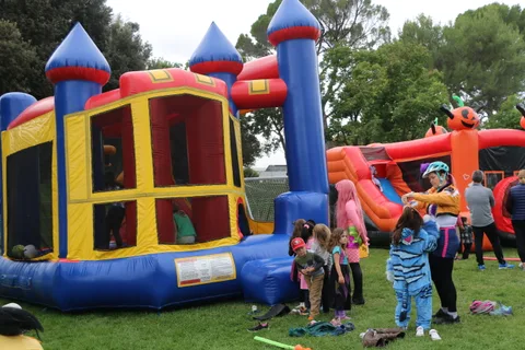 Children play around a colorful inflatable bounce house castle in the park.