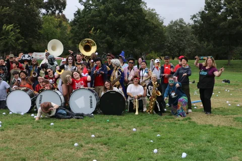 A marching band poses with drums and brass instruments on the grass at the festival.