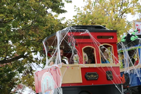 A red trolley car decorated with spiderwebs sits on the parade route.